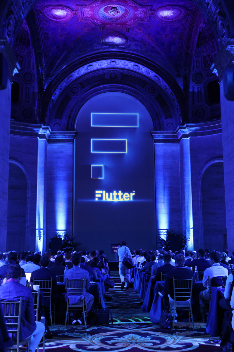 A Flutter event with people sitting in front of a stage with the Flutter logo illuminated by a blue light