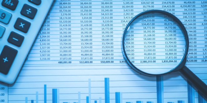 Magnifying glass over numbers next to a calculator, symbolic of the audit KPMG has done of Norway's Norsk Tipping