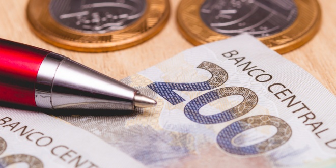 Brazilian money with a pen next to it, counting Brazil taxes